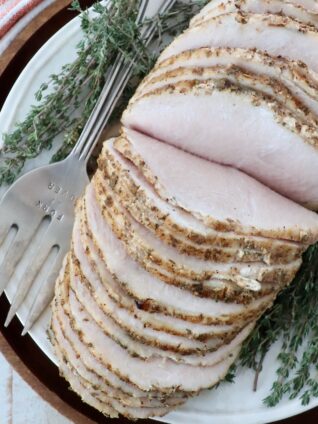 sliced turkey breast on a plate with fresh thyme and a serving fork