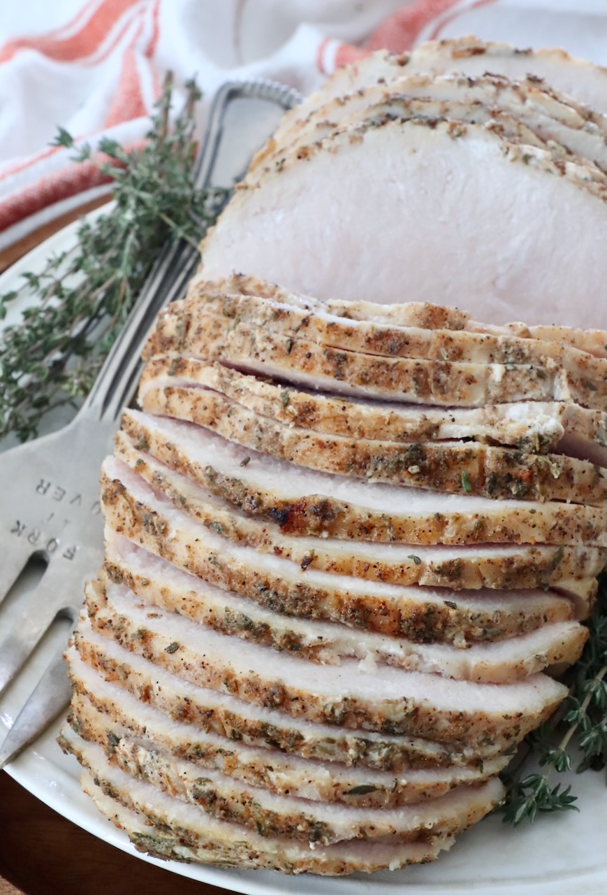 sliced turkey breast on a plate with a serving fork and fresh thyme sprigs