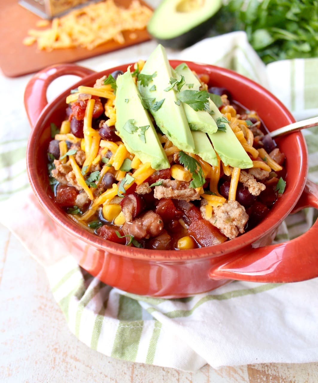 A red bowl filled with turkey taco soup topped with shredded cheese and avocado. 