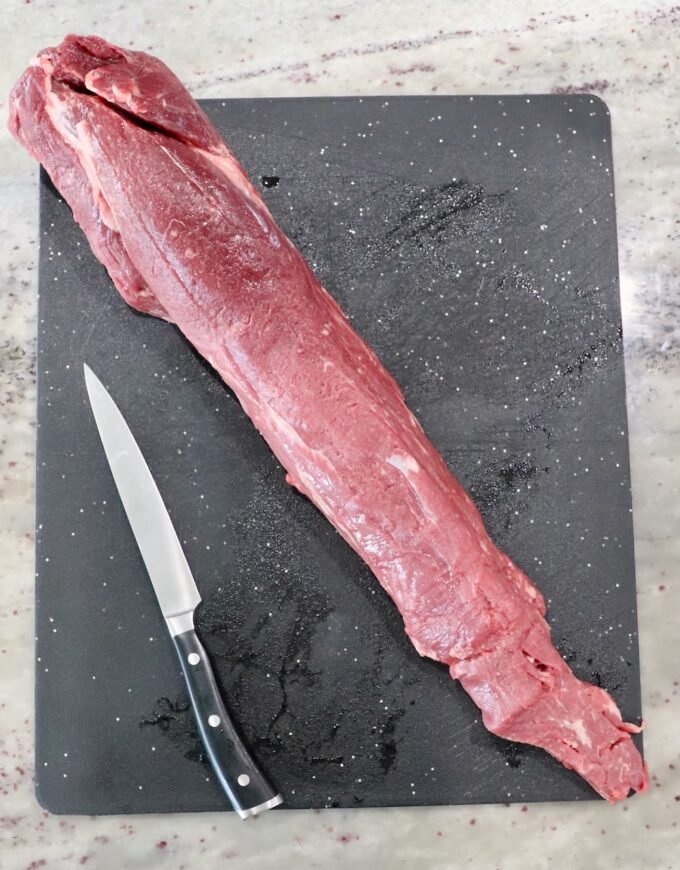 whole beef tenderloin on a cutting board with a knife