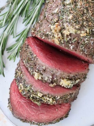 sliced beef tenderloin on a plate with fresh rosemary