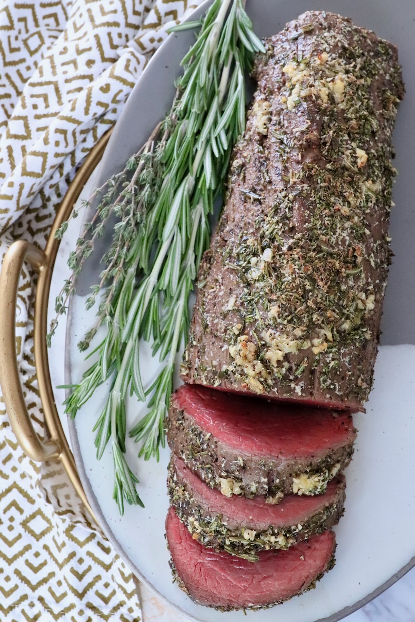 herb rubbed beef tenderloin on a plate with fresh herbs