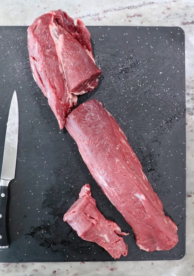 beef tenderloin cut into three sections on a cutting board with a knife