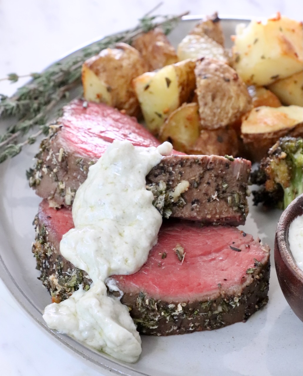 gorgonzola cream sauce  on top of slices of beef tenderloin on a plate with roasted potatoes