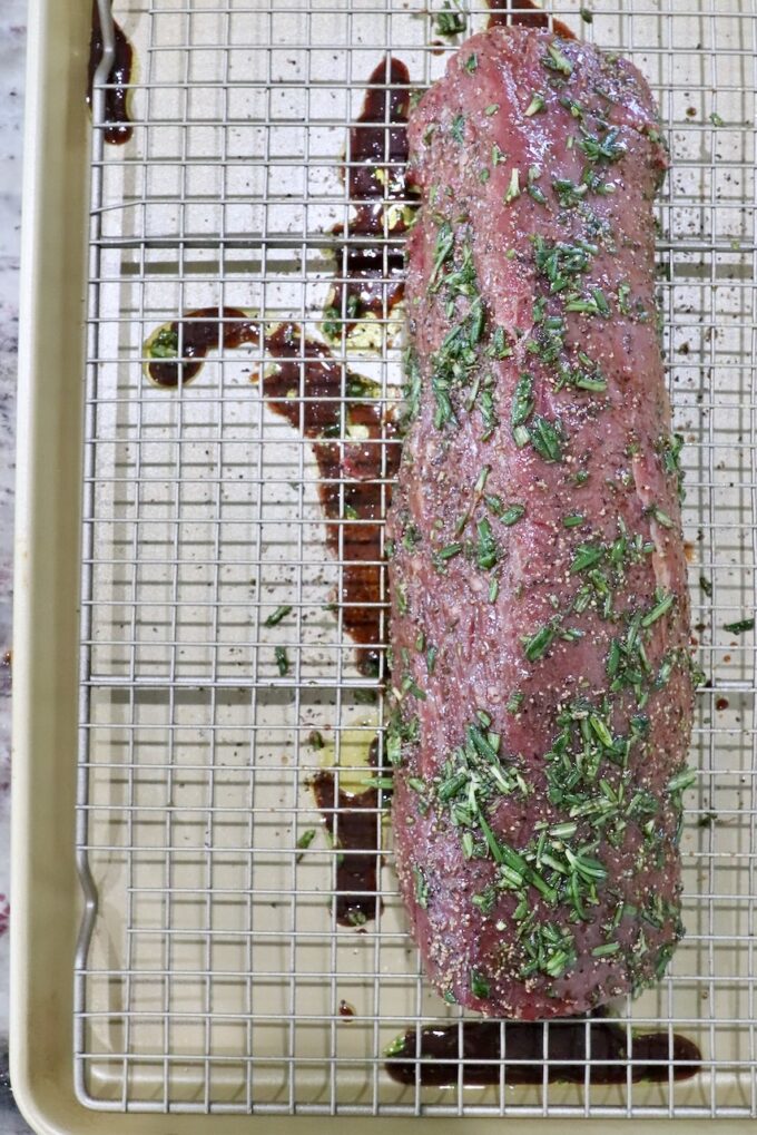 herb rubbed beef tenderloin on a wire rack over a rimmed baking sheet