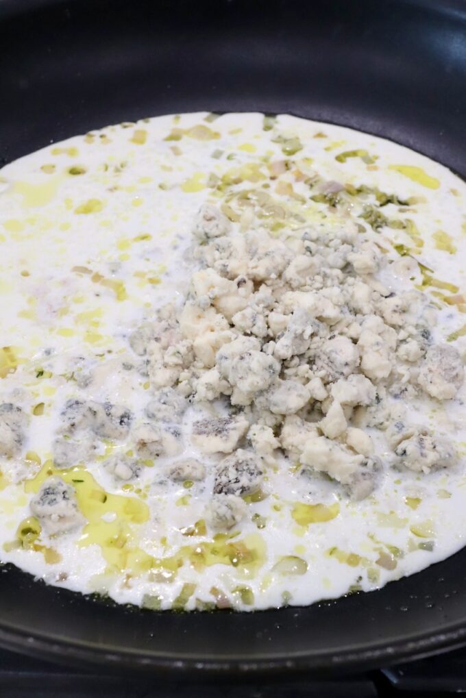 gorgonzola crumbles on top of a cream sauce in a skillet