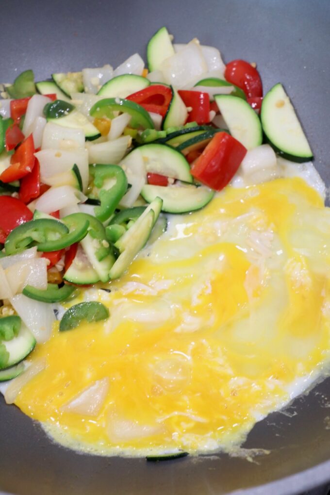 cooked sliced vegetables in wok with whisked eggs