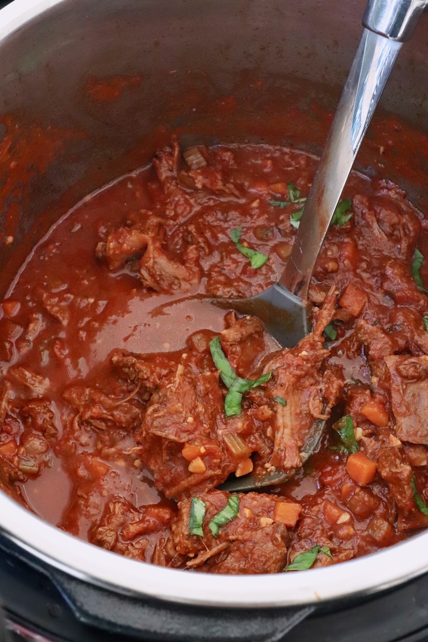 shredded beef ragu sauce in an Instant Pot with a serving spoon