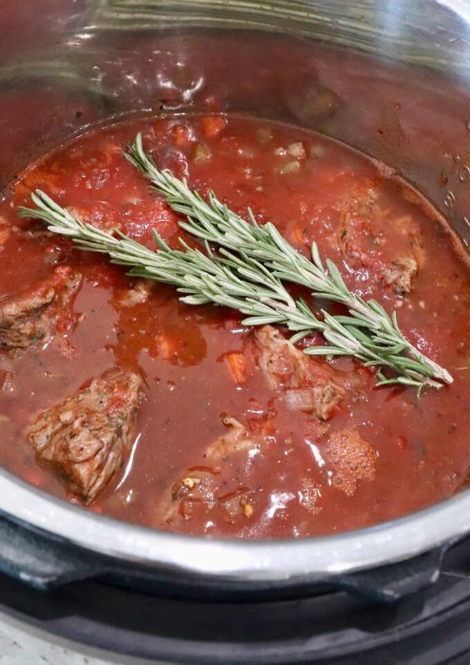 beef ragu sauce in Instant Pot topped with sprigs of rosemary