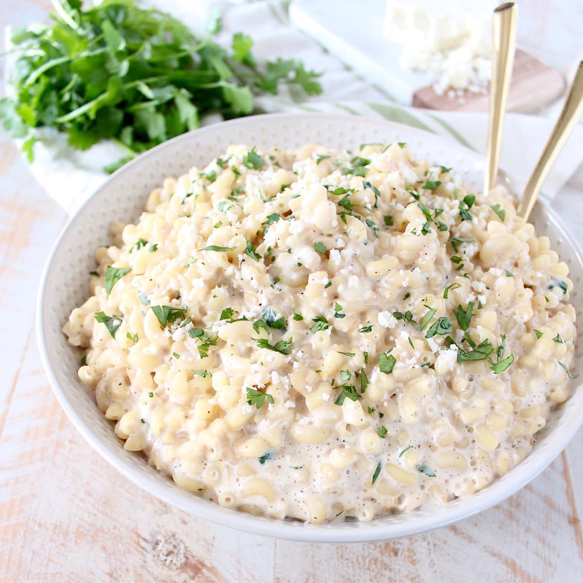 Mexican street corn mac and cheese in a white bowl with gold serving spoons. 