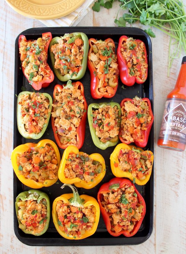 Overhead shot of buffalo chicken stuffed bell peppers on baking sheet with bottle of buffalo sauce on the side
