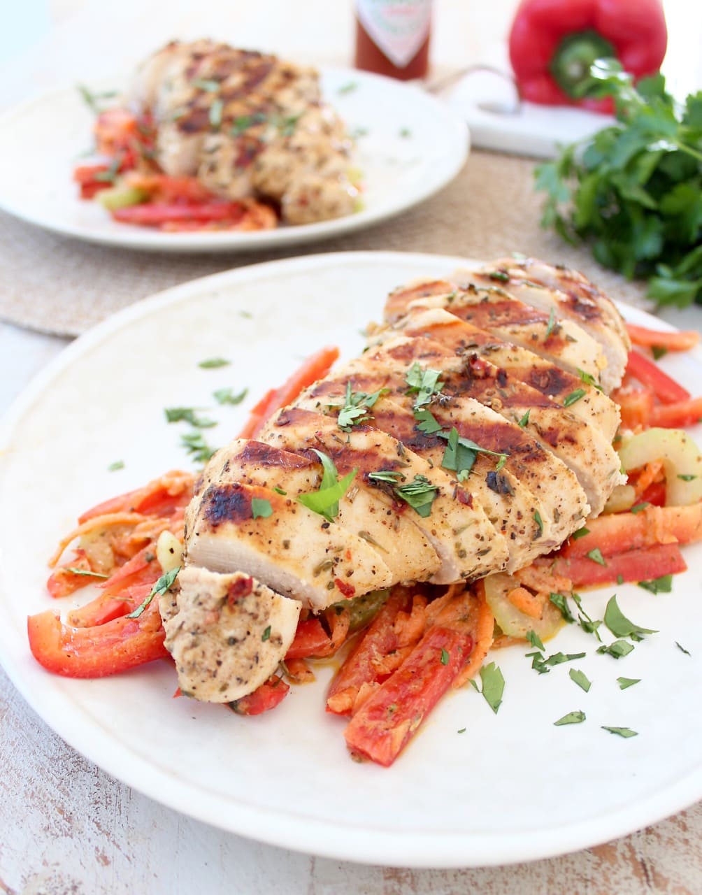 A white plate topped with sliced red bell peppers and a sliced chicken breast garnished with herbs.