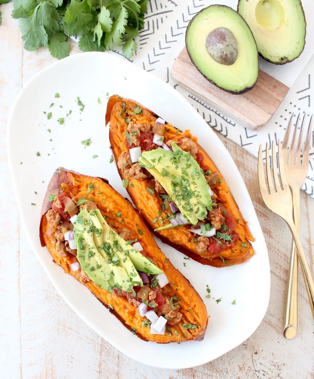 baked sweet potato cut in half and topped with chili and sliced avocado on a white plate