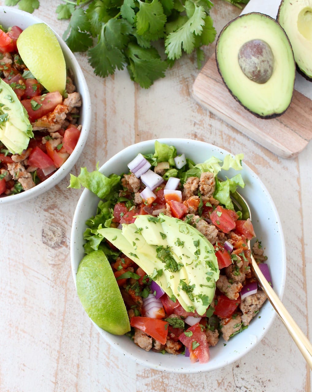 A white bowl on a wooden surface filled with Taco seasoned ground turkey cooked with peppers, onions and tomatoes on top of lettuce.