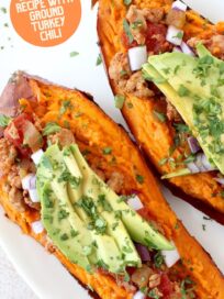 baked sweet potato cut in half on plate topped with chili, sliced avocado and chopped cilantro