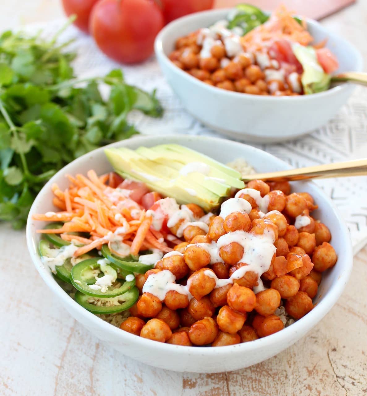 bowls filled with chickpeas tossed in buffalo sauce and sliced vegetables and a gold fork in the bowl