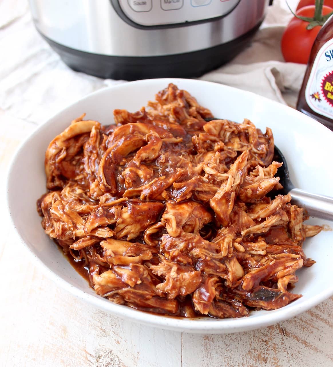 Shredded BBQ chicken in a white bowl with a spoon.