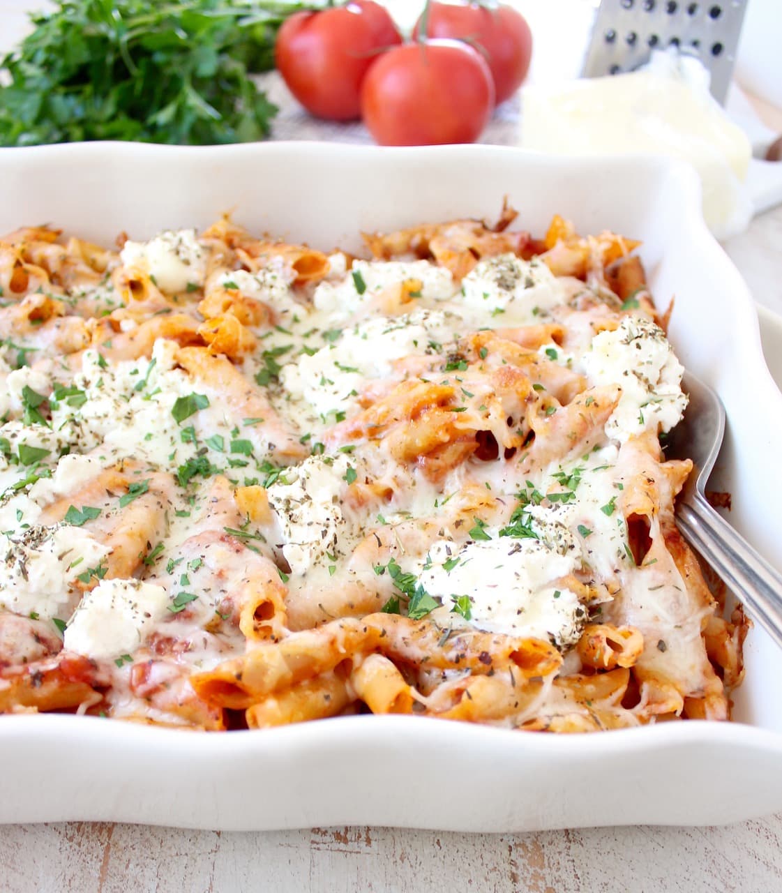 baked ziti in casserole dish topped with ricotta cheese and herbs