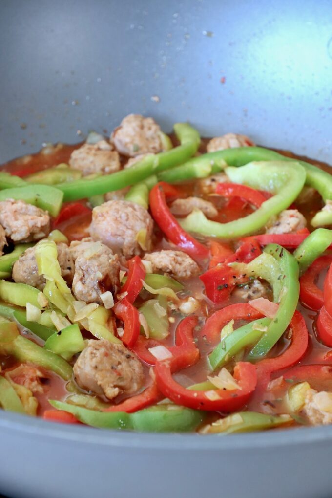 sliced bell peppers and Italian sausage in broth in large pan