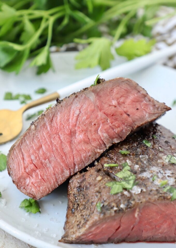 sous vide steak sliced in half on plate with fork and fresh parsley