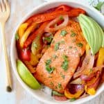 Baked Salmon with Fajita Seasoned Bell Peppers and Onions in Bowl with Sliced Avocado and Lime Wedge