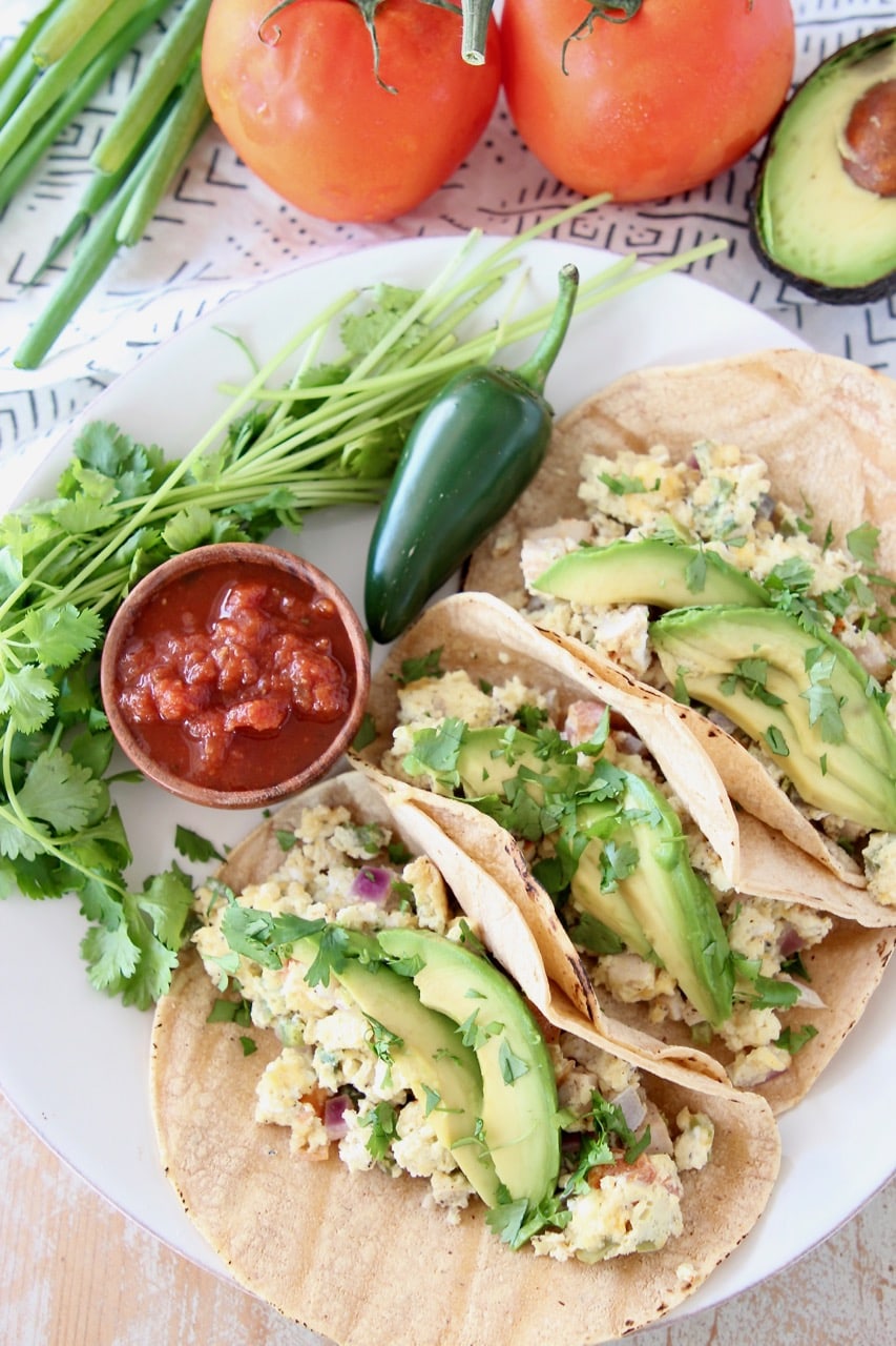 Egg, veggie, cheese breakfast tacos with sliced avocado, jalapeno and small cup of salsa