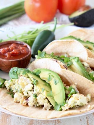 Breakfast egg tacos on corn tortillas with sliced avocado and cilantro