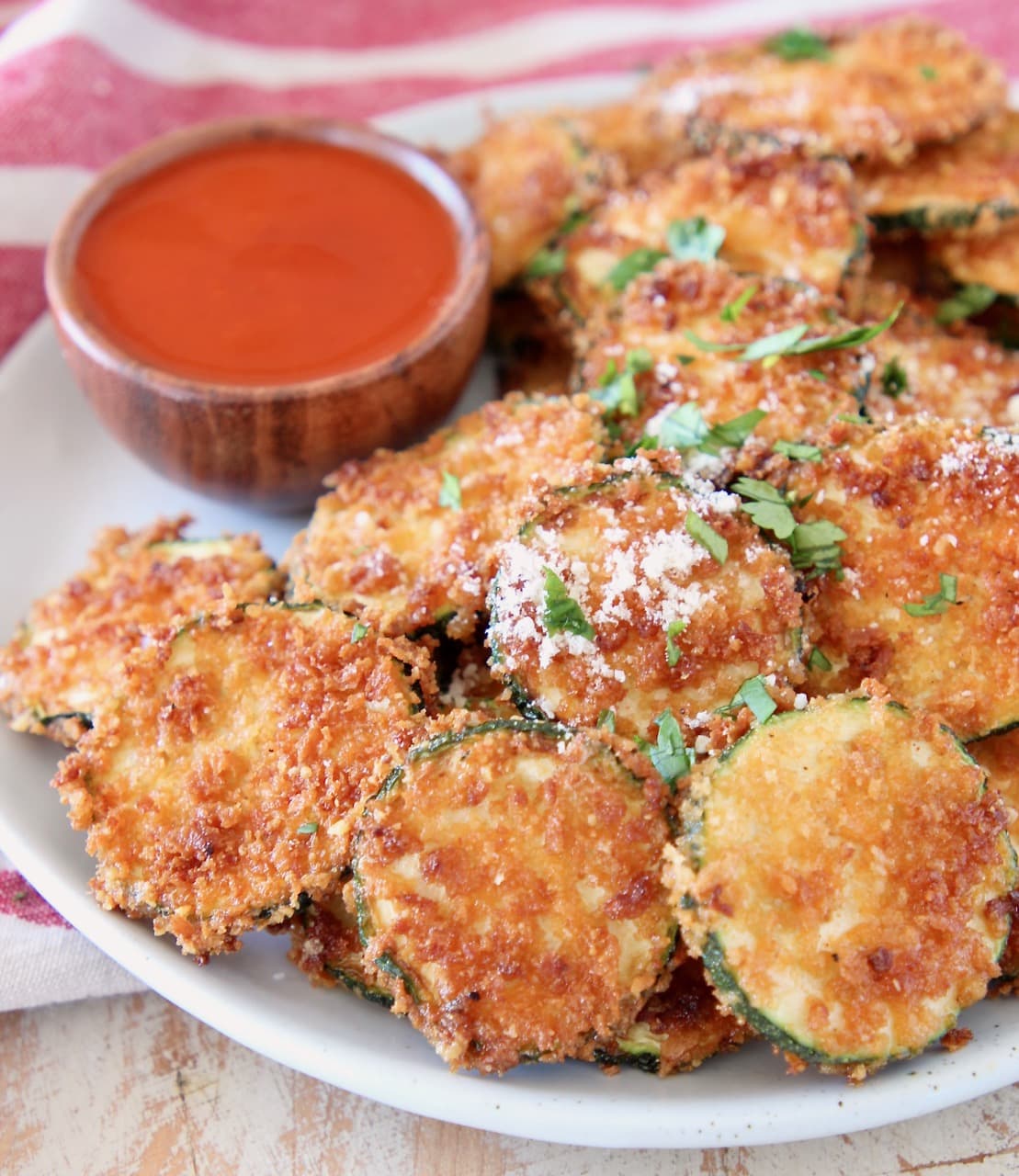 Crispy fried zucchini chips with parmesan cheese on a plate with small wooden bowl of buffalo sauce