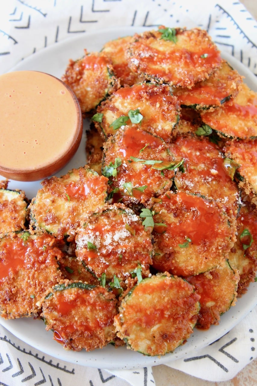 Crispy Zucchini Chips drizzled with buffalo sauce on plate with small bowl of buffalo blue cheese dressing