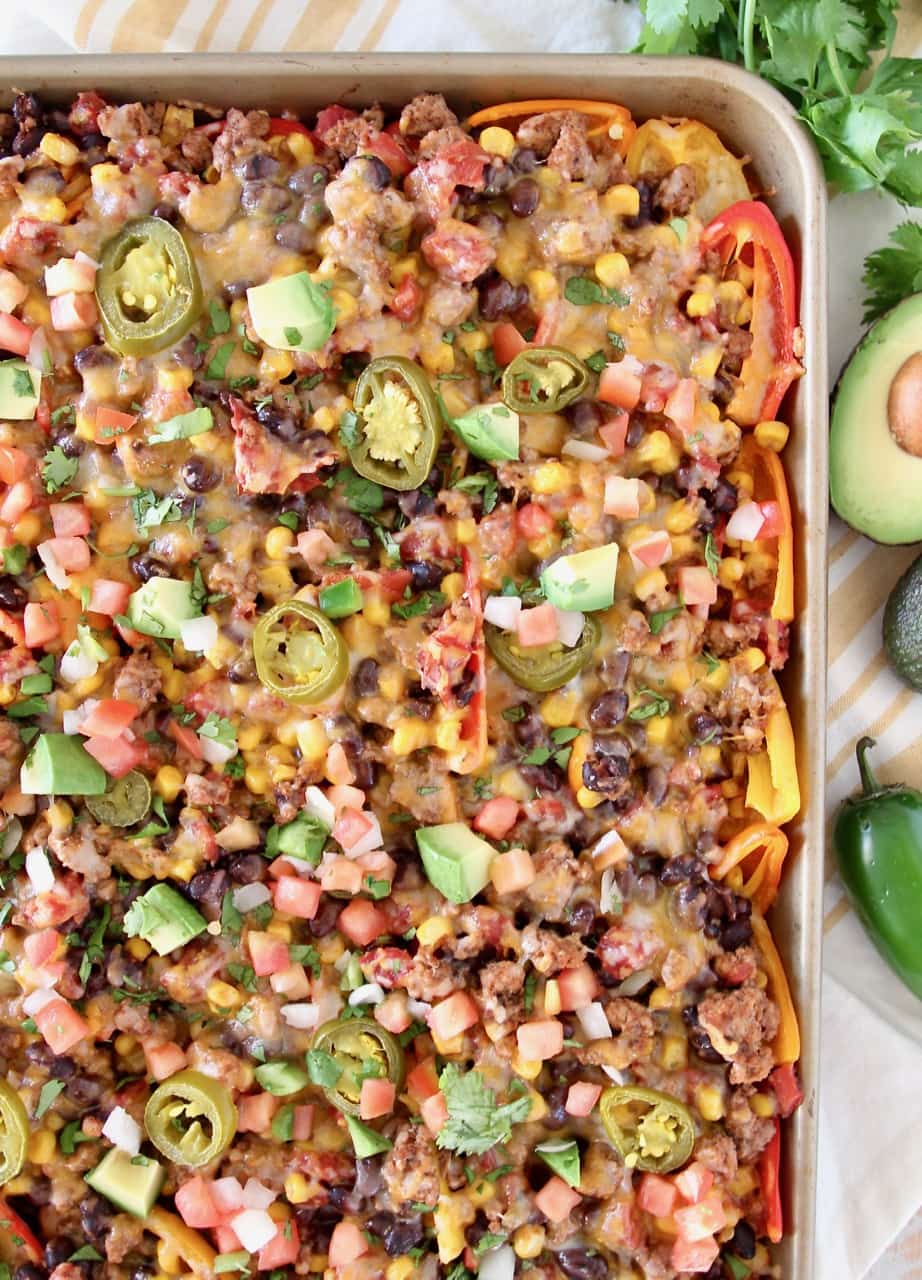 Low carb nachos on a baking sheet with avocado and jalapeno