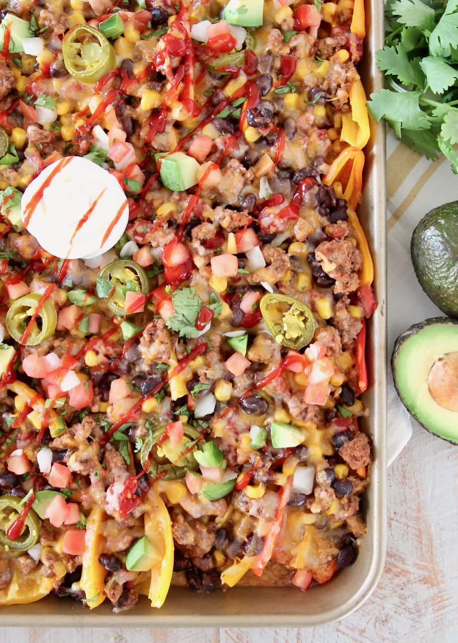 Low Carb Nachos made with sweet mini bell peppers, topped with turkey, beans, corn, tomatoes, jalapenos, avocado, hot sauce and sour cream on a baking sheet