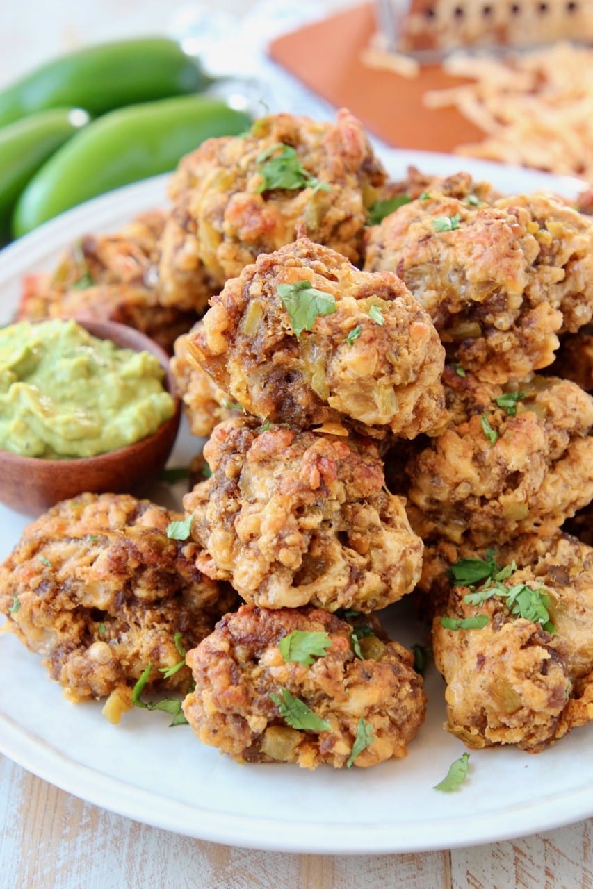 sausage balls piled up on plate with small bowl of avocado dipping sauce