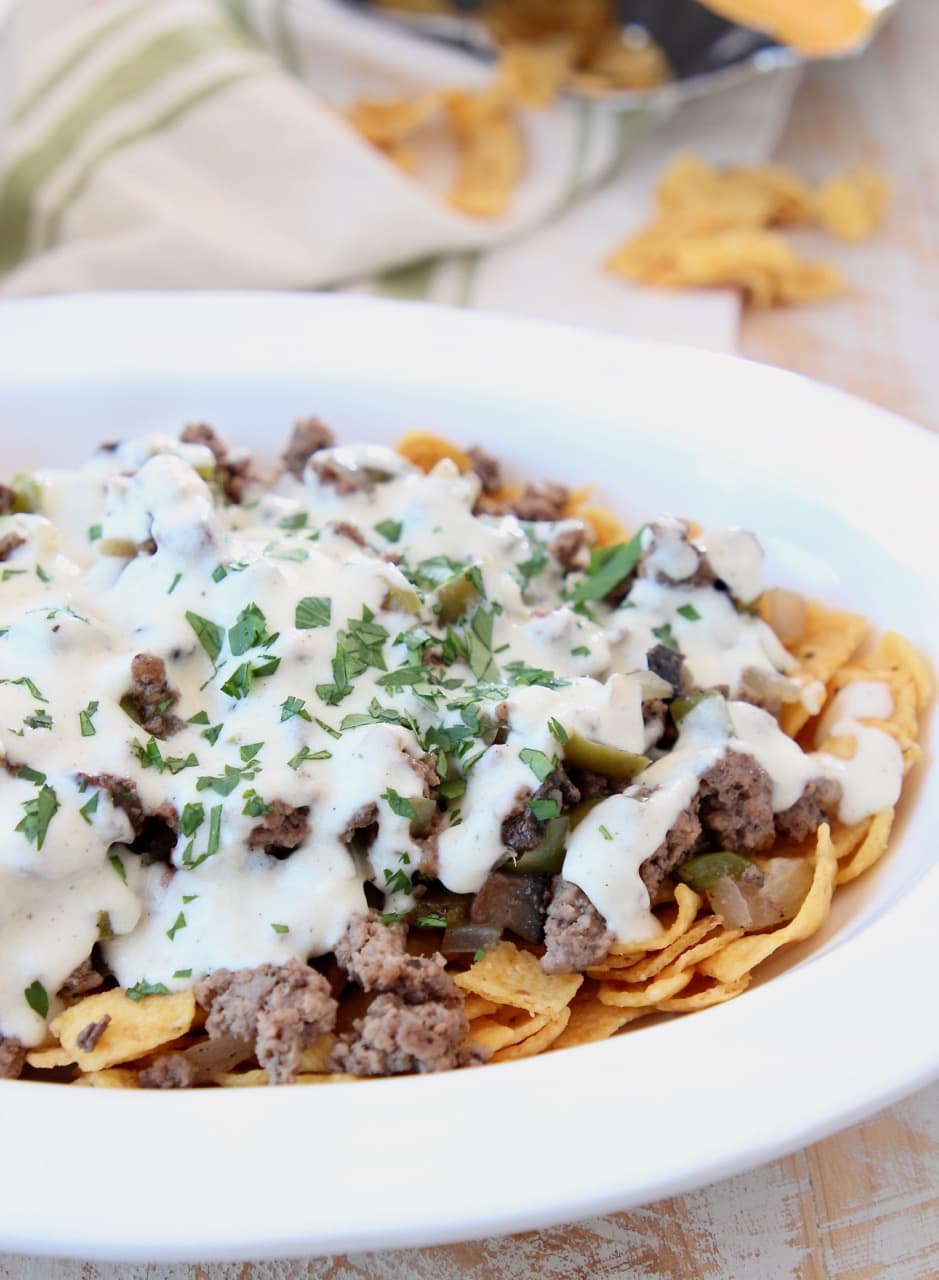 Fritos topped with ground beef and creamy provolone sauce in casserole dish