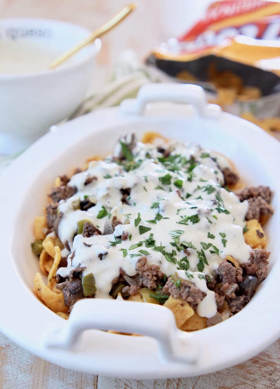 Philly Cheesesteak Frito Pie topped with Creamy Provolone Cheese Sauce in white casserole dish