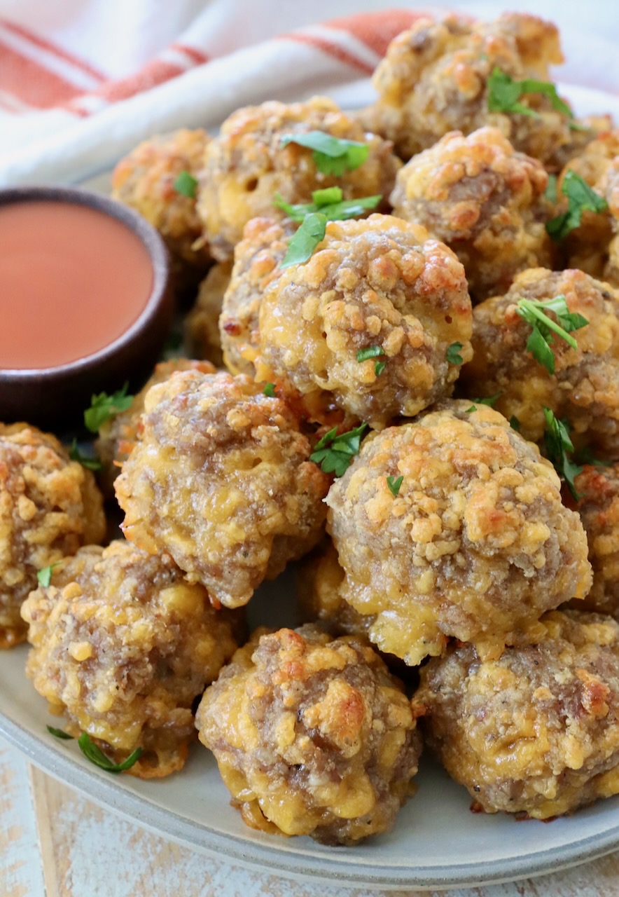sausage balls stacked up on a plate with a small bowl of buffalo sauce on the side