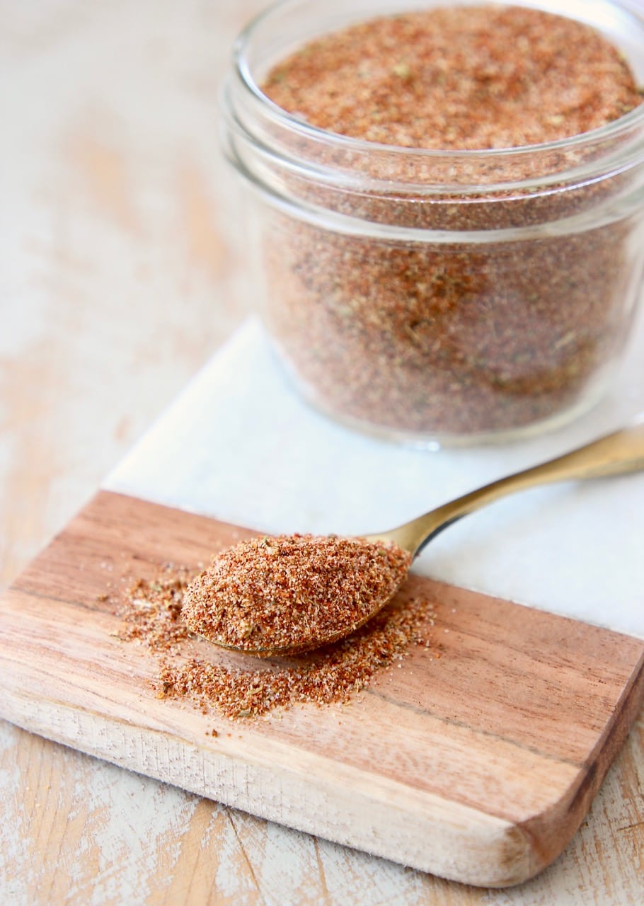 Homemade taco seasoning in mason jar on marble cutting board with spoon of taco seasoning