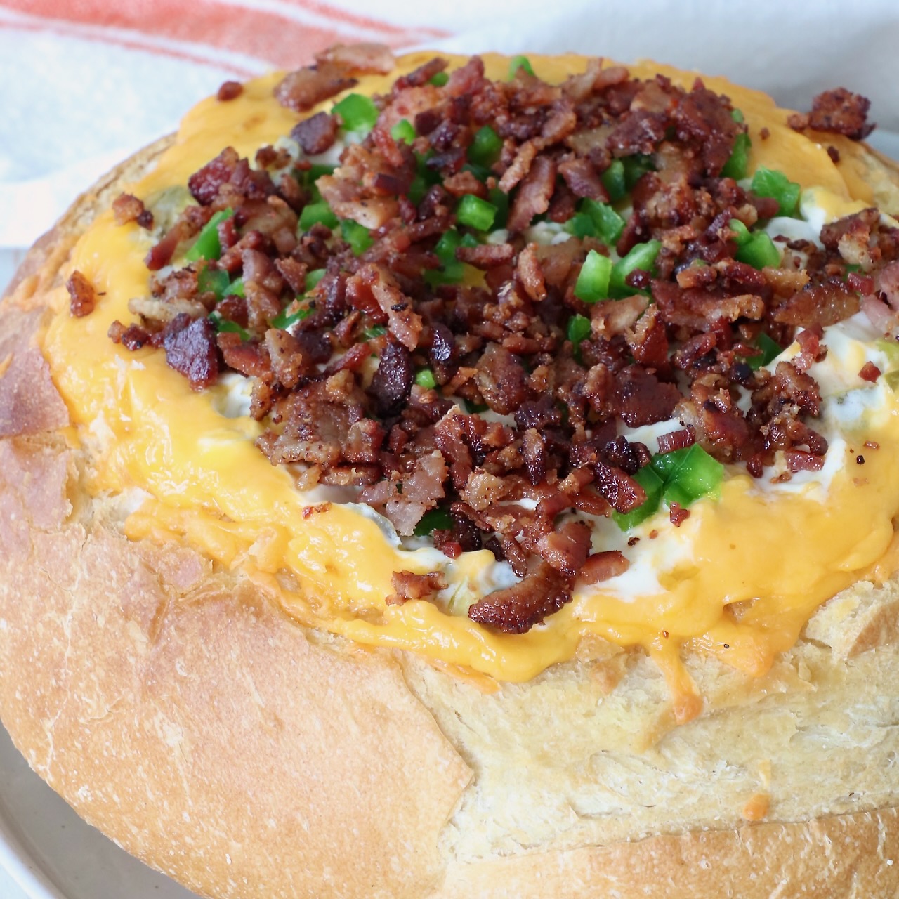 Round bread loaf hollowed and filled with melted cheese, topped with crispy bacon bits and chopped green peppers