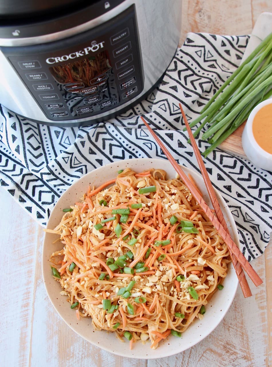 Pressure cooker chicken noodles with thai peanut sauce in bowl with chopsticks, next to Crock Pot Express Crock machine