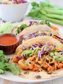 Buffalo cauliflower tacos on corn tortillas with jalapeno carrot slaw and fresh cilantro on plate with small bowl of buffalo sauce