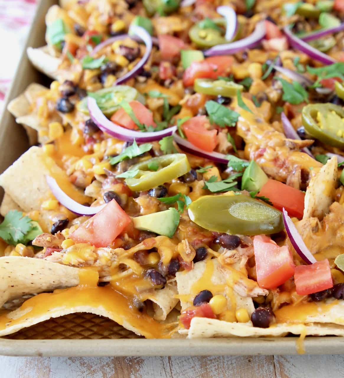 Sheet pan of chicken nachos with black beans, cheese, tomatoes, sliced jalapenos, red onions and avocado