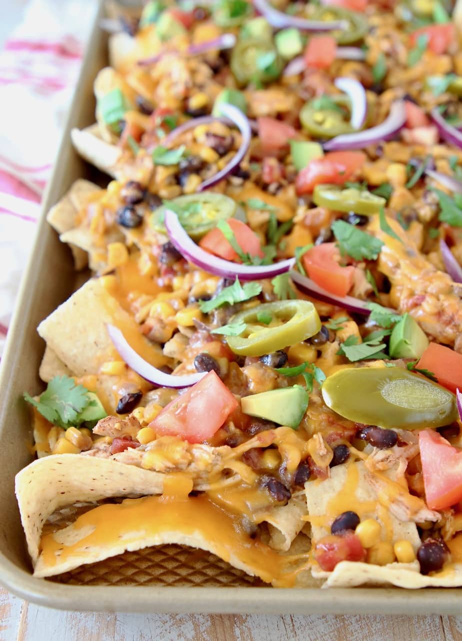 Chicken nachos on sheet pan with melted cheese, sliced nacho jalapenos, diced tomatoes and sliced red onions