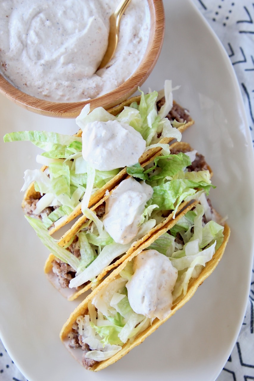 Ground beef tacos in crispy shells with shredded lettuce and french onion dip on plate with bowl of french onion dip