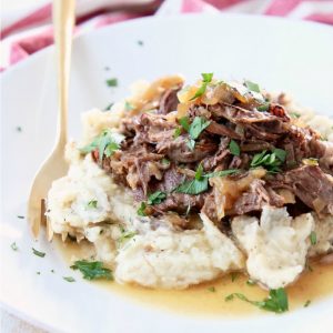 French onion pot roast on mashed potatoes with fresh parsley on white plate with gold fork