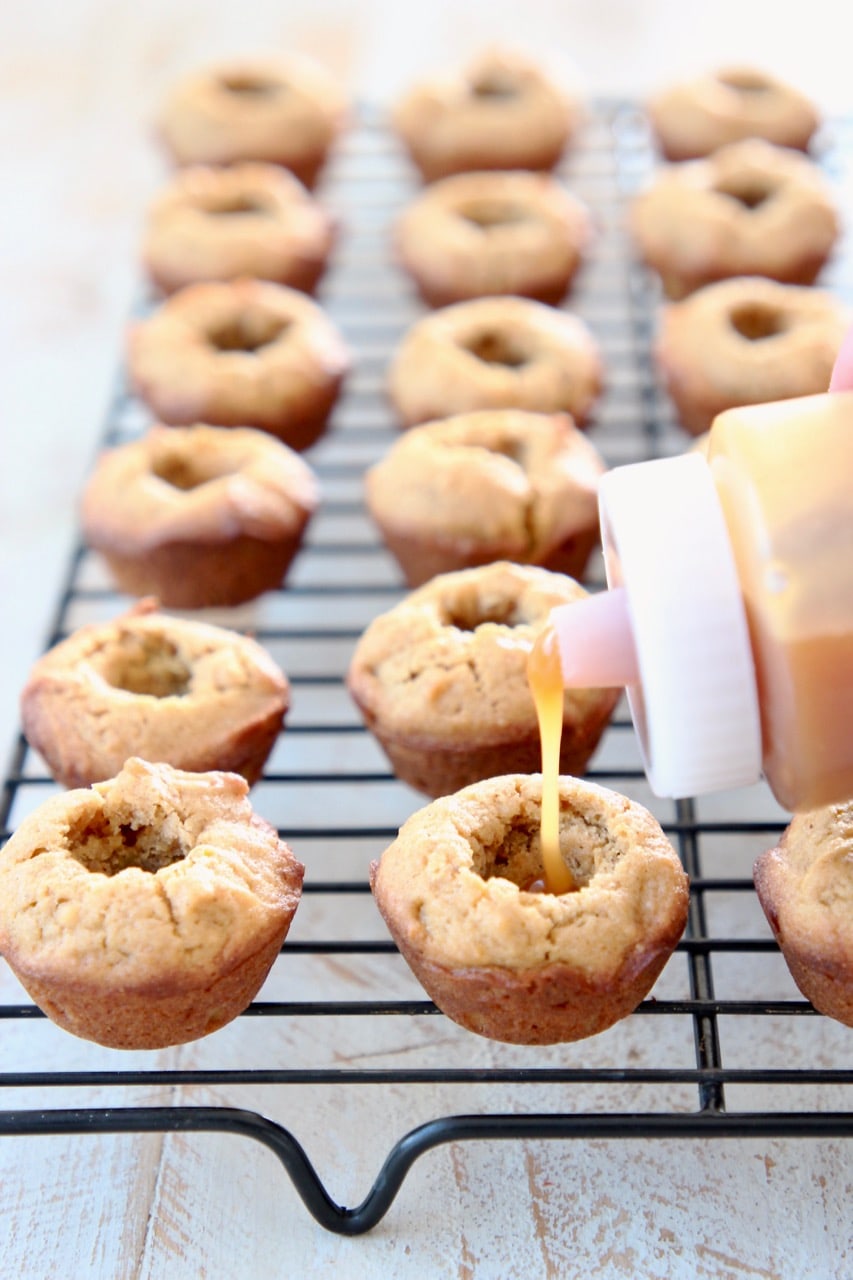 Plastic squeeze bottle with salted caramel sauce, filling mini pumpkin cookie cups on black wire baking rack