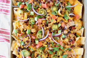 The best chicken nachos, image of nachos on sheet pan with text overlay "The Best Chicken Nachos - Easy Crock Pot Recipe"