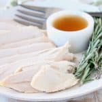 Sliced turkey breast on white plate with maple apple reduction in small white ramekin, large fork on side of plate and fresh rosemary sprigs