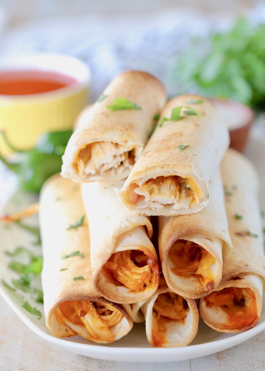 Buffalo chicken taquitos stacked up on plate with top taquito cut in half, garnished with fresh cilantro