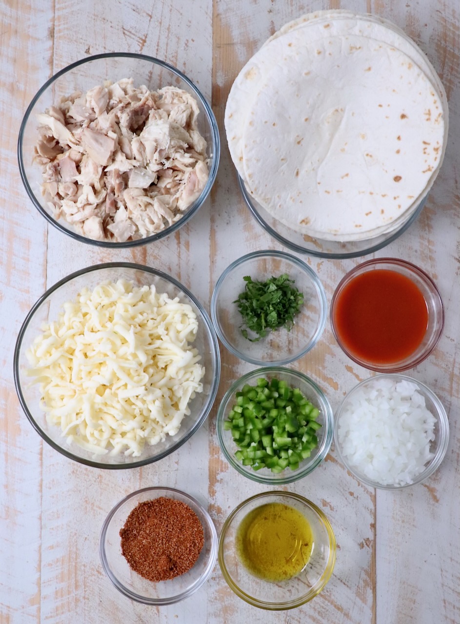 ingredients for buffalo chicken taquitos on a white wood board