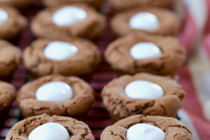 Chocolate cookies formed into cups filled with marshmallow creme on black wire baking rack