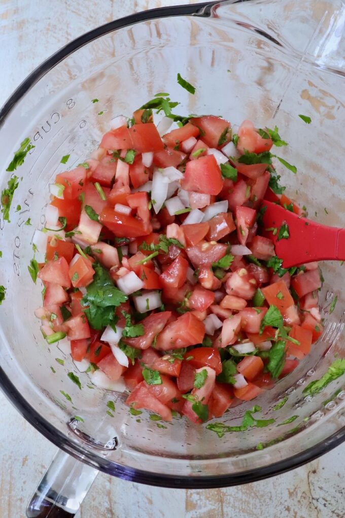 pico de gallo in a glass bowl with a red spatula